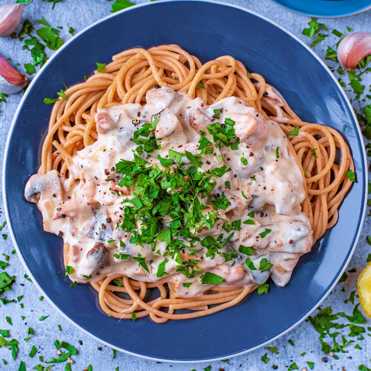 A blue plate with creamy mushroom pasta on it.