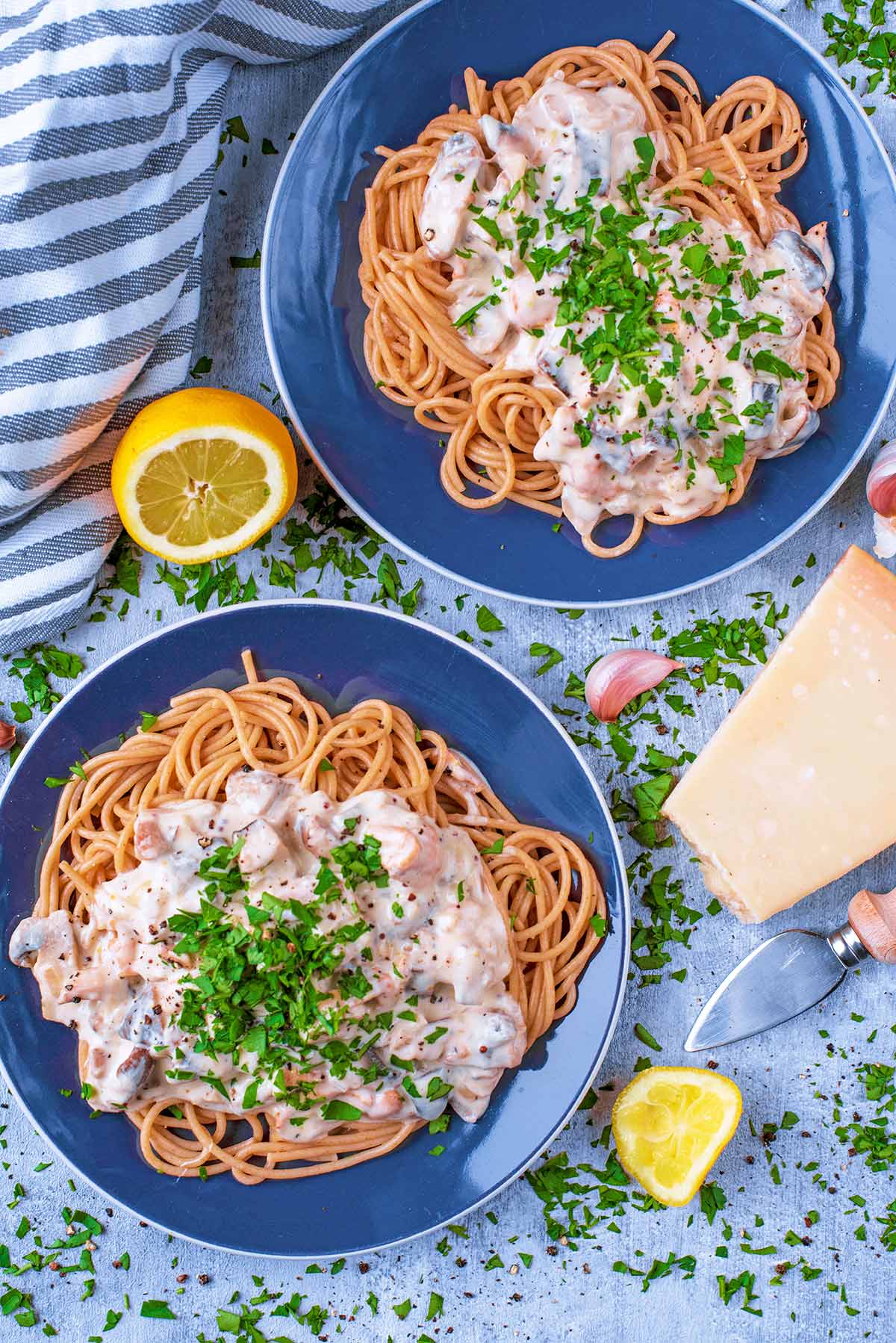 Two blue plates with creamy mushroom spaghetti. Parmesan and lemons are next to them.