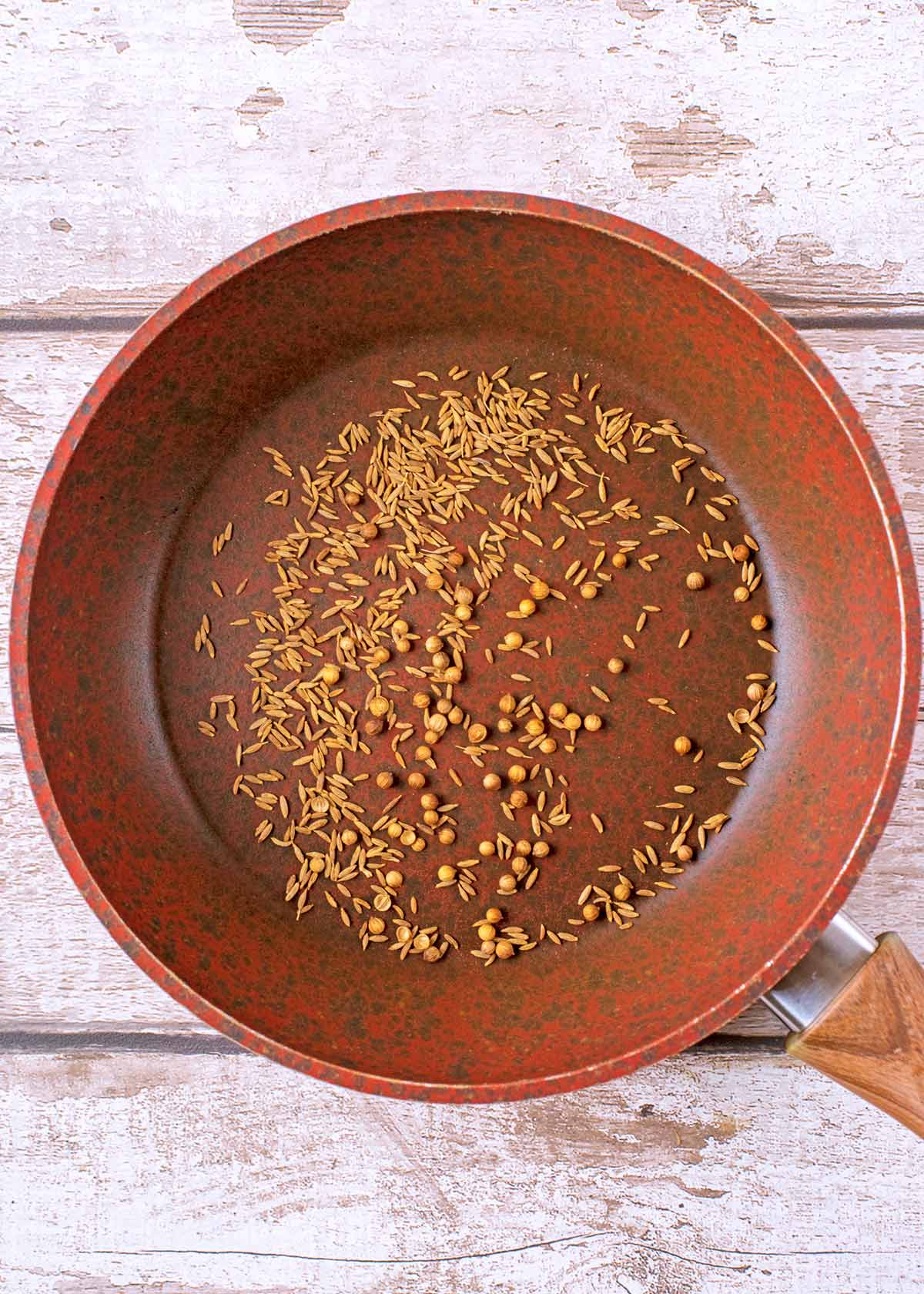 A frying pan with cumin seeds and coriander seeds.
