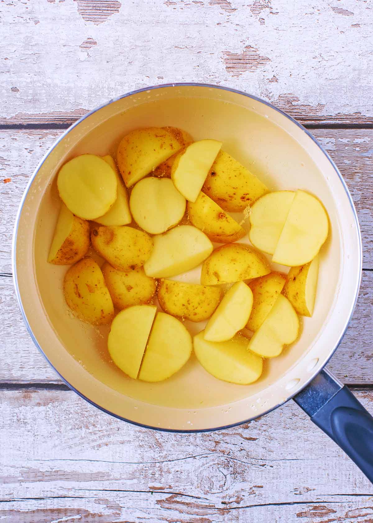 A saucepan containing baby potatoes cut in half.