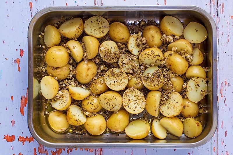 A roasting tin full of halved new potatoes covered in minced garlic and herbs.