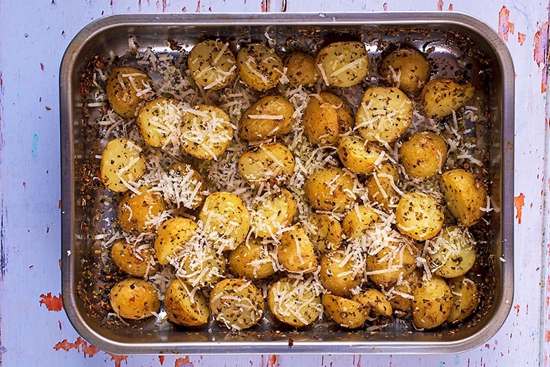 A roasting tin full of roasted potatoes covered in parmesan