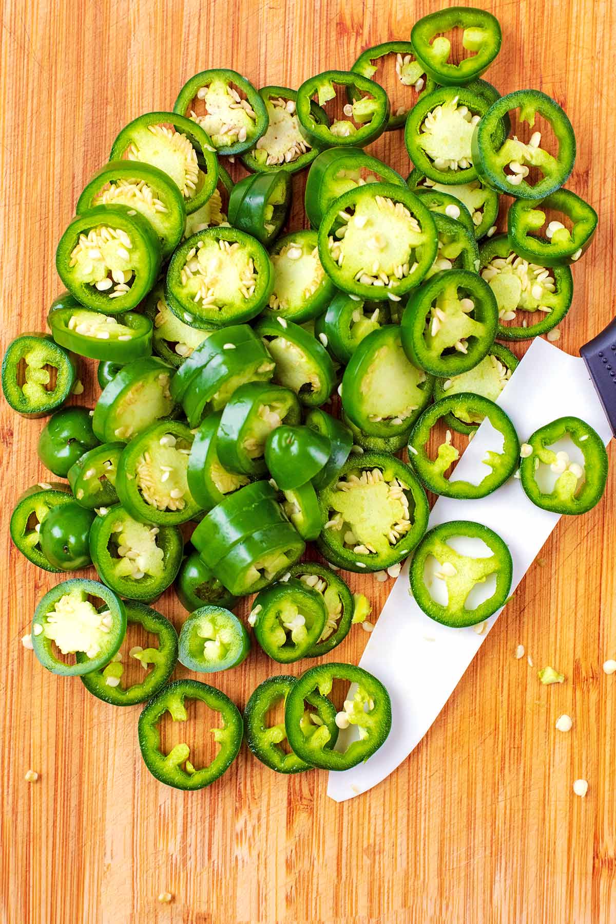 Sliced jalapenos on a wooden chopping board.