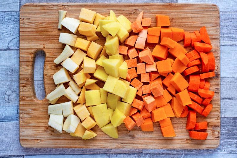 a selection of root vegetables chopped into cubes on a chopping board.