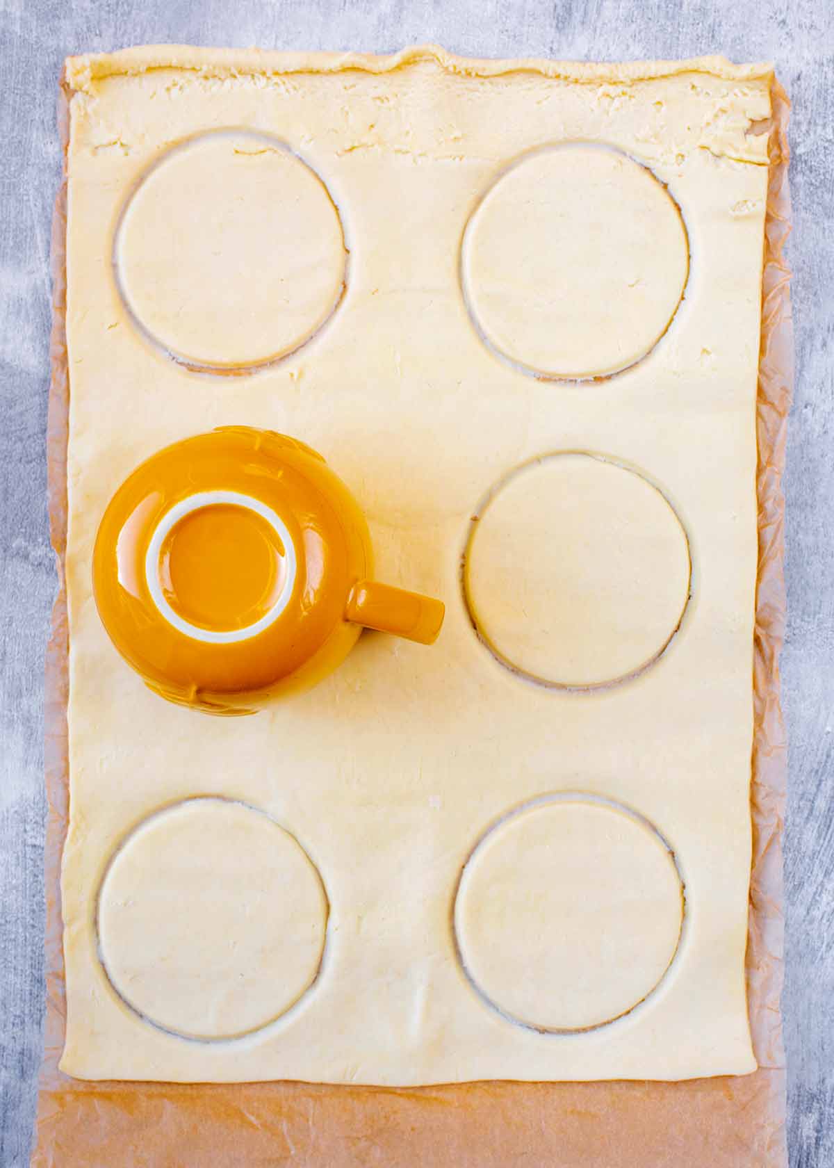 A large sheet of pastry with a mug being used to cut circles.