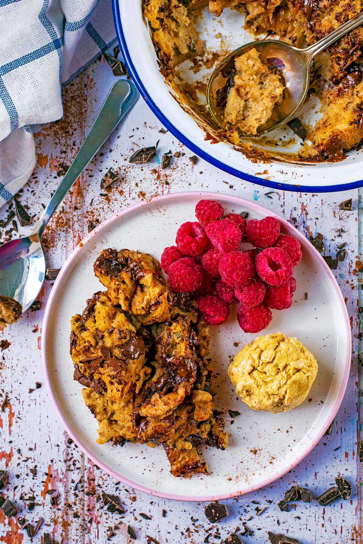 Bread pudding on a white plate next to a serving spoon and a towel.