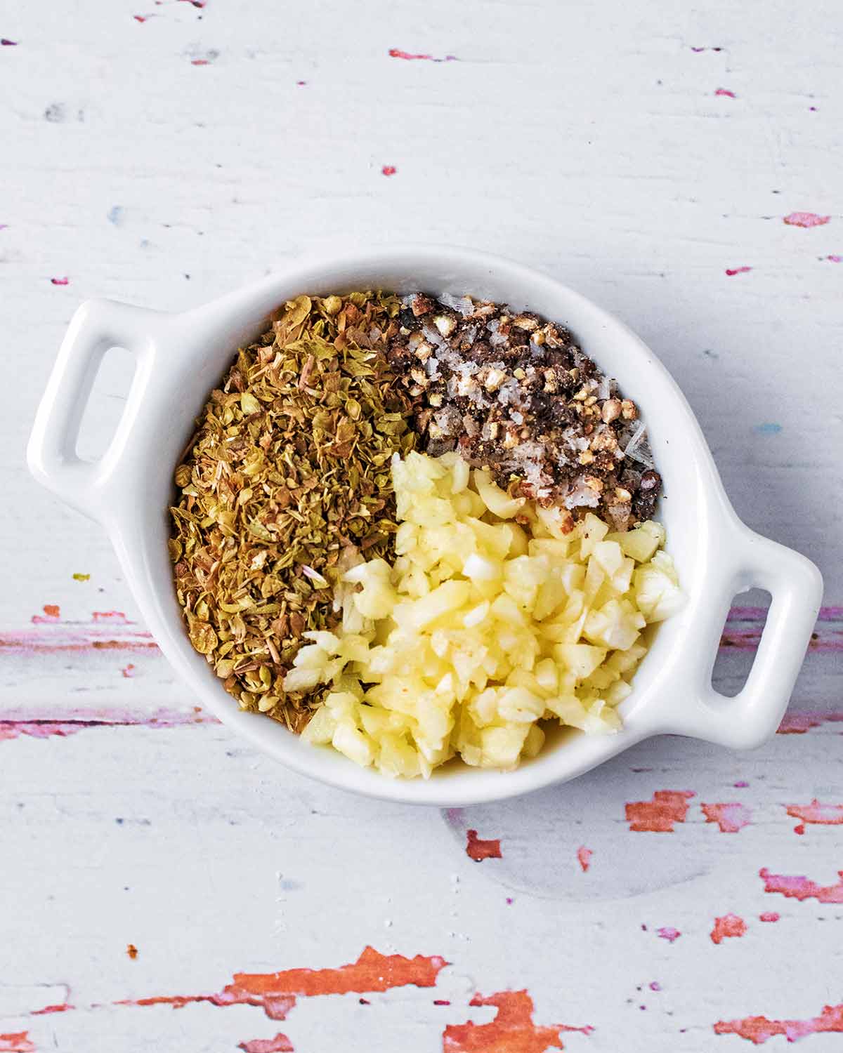 A small dish containing salt, pepper, oregano and minced garlic.