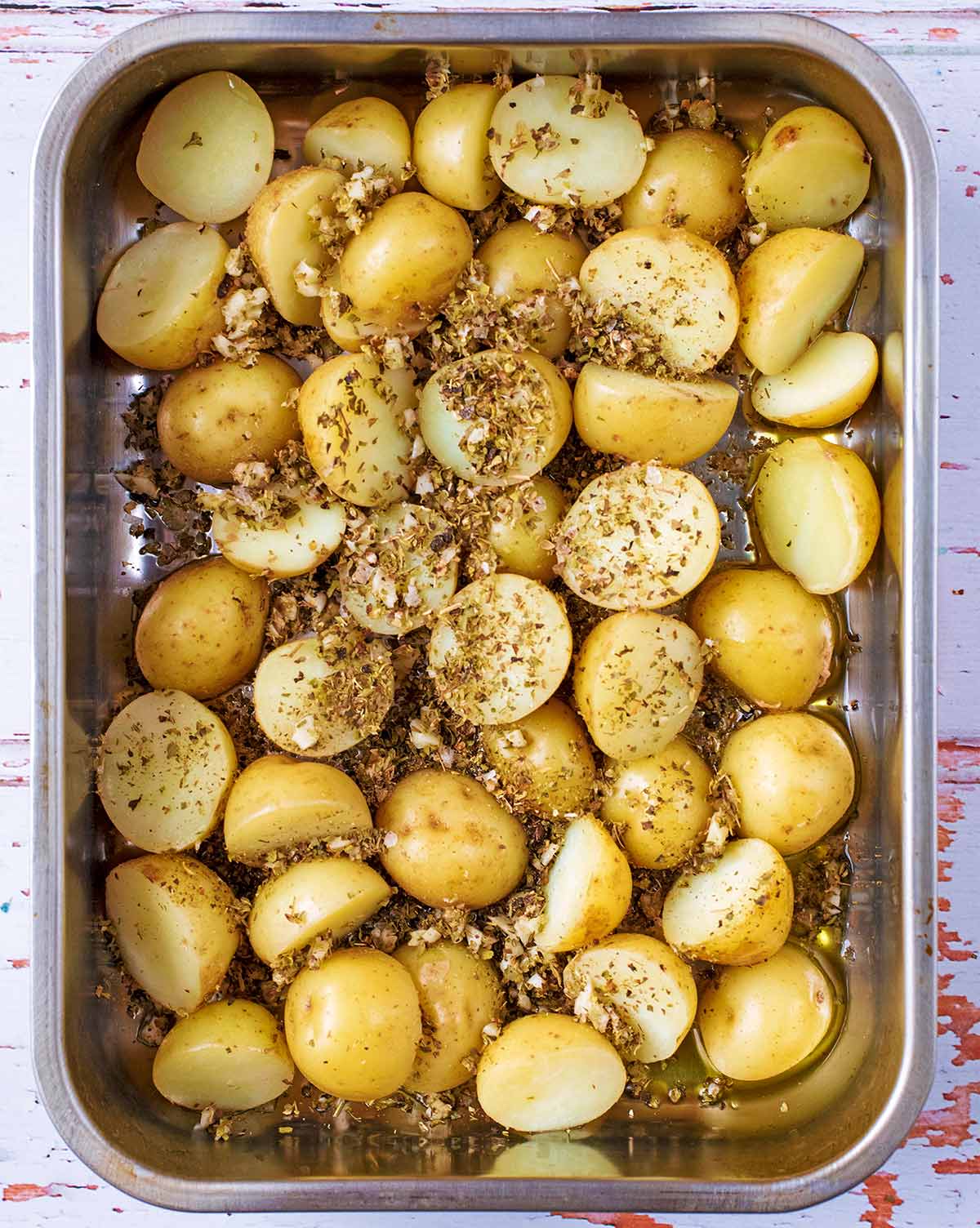 A roasting tin full of halved new potatoes covered in minced garlic and herbs.