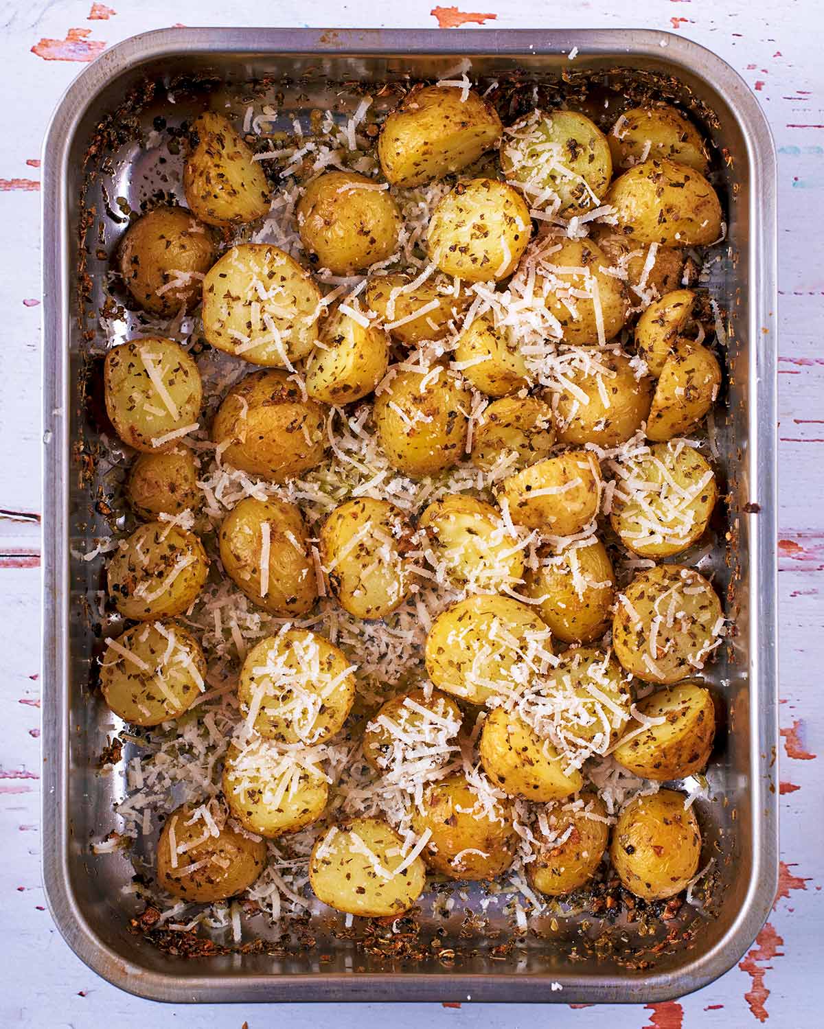 A roasting tin full of roasted potatoes covered in parmesan.