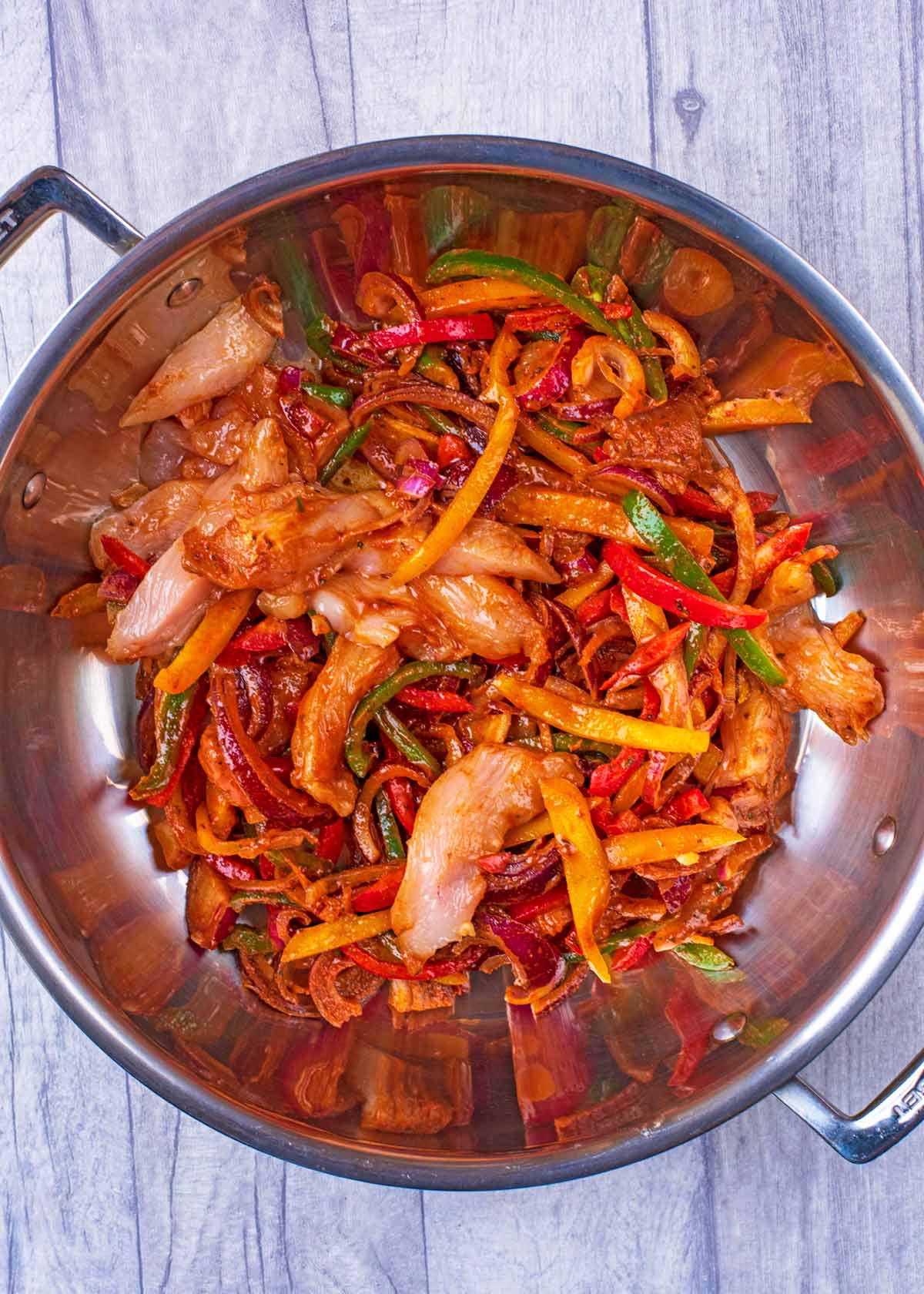 Raw marinated chicken and strips of pepper and onion in a large pan.