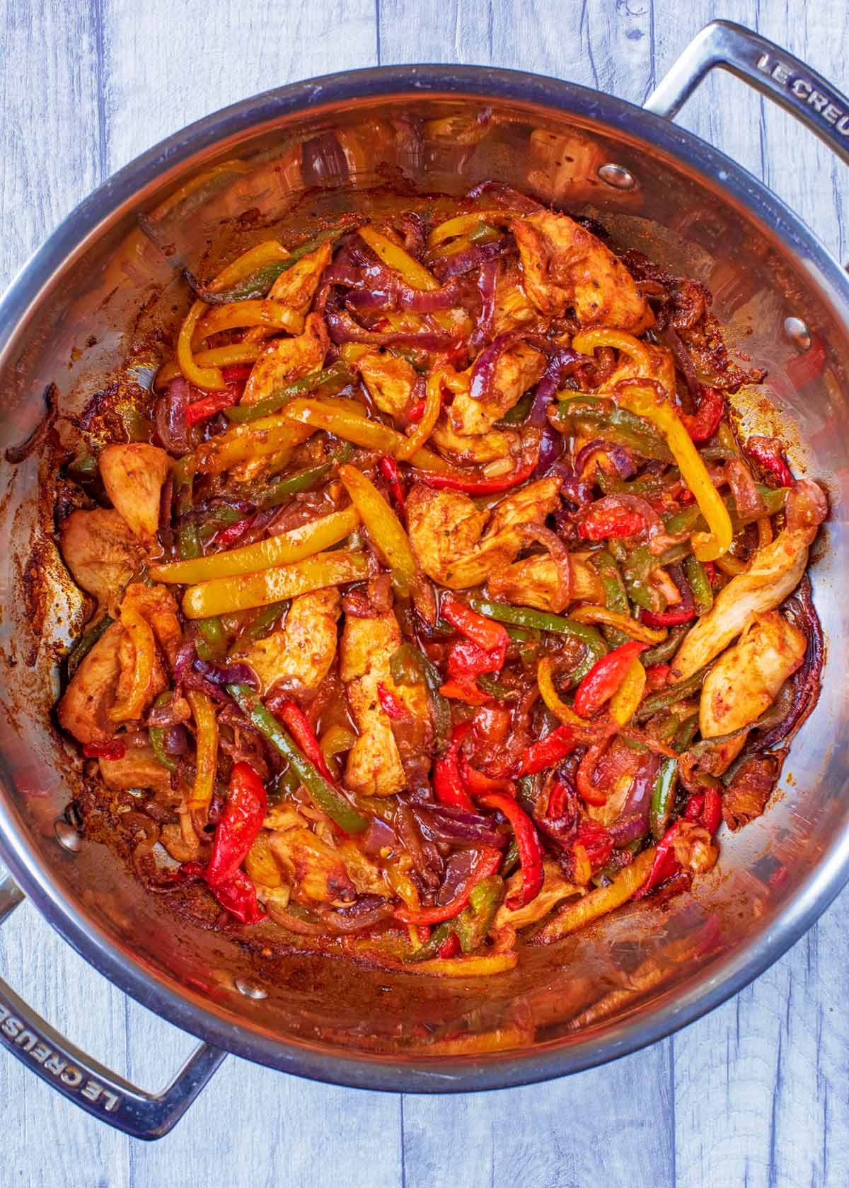 Cooked chicken, peppers and onions in a large silver pan.