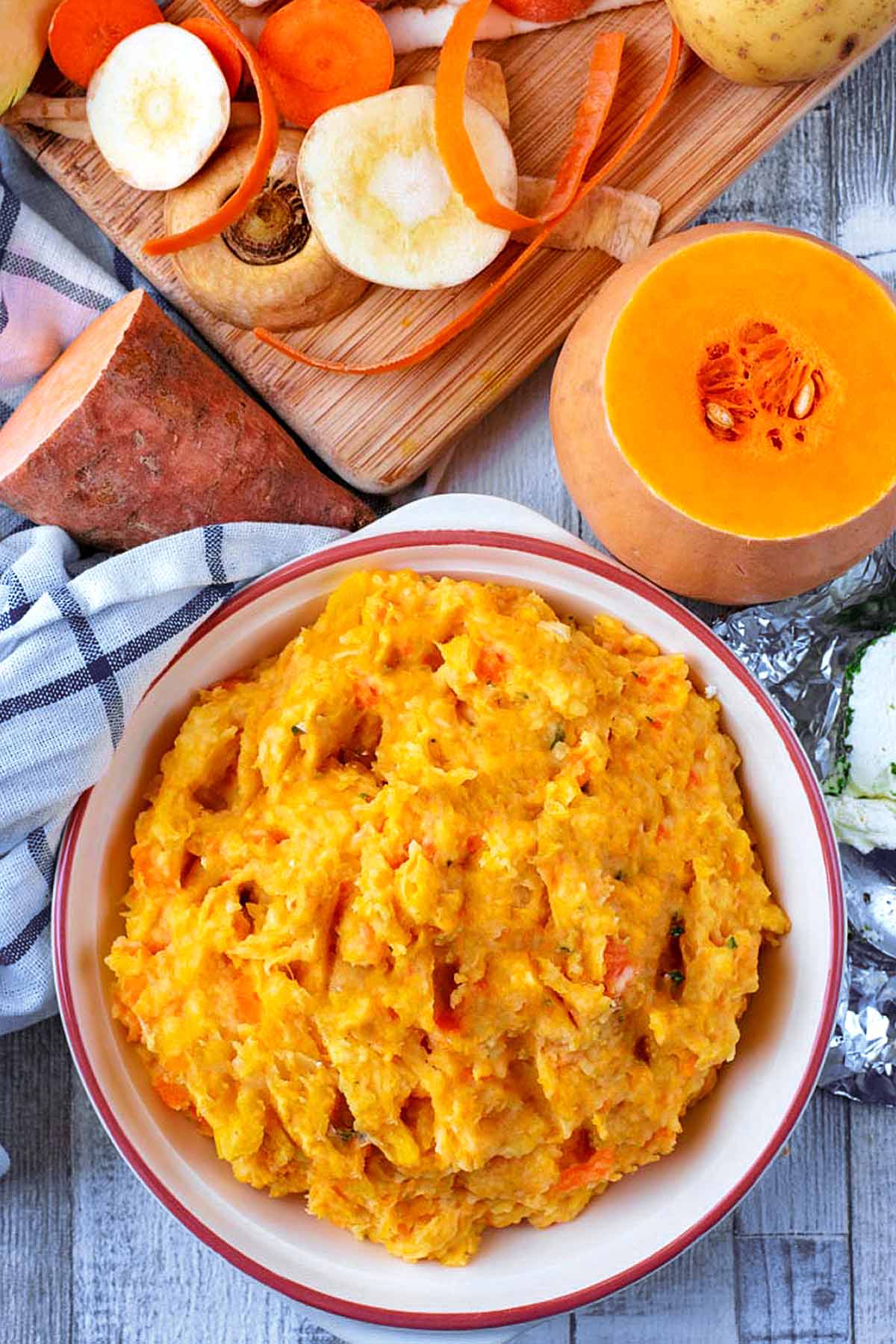 Mash in a bowl next to a chopping board and various chopped root vegetables.