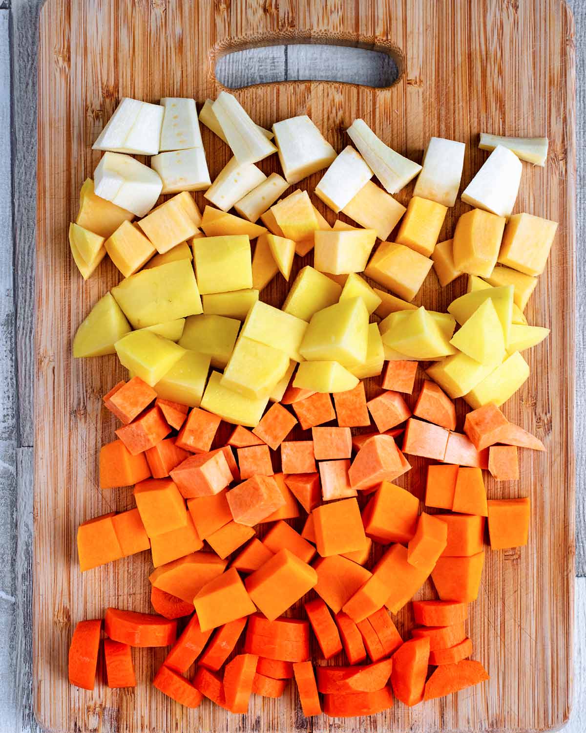 A selection of root vegetables chopped into cubes on a chopping board.