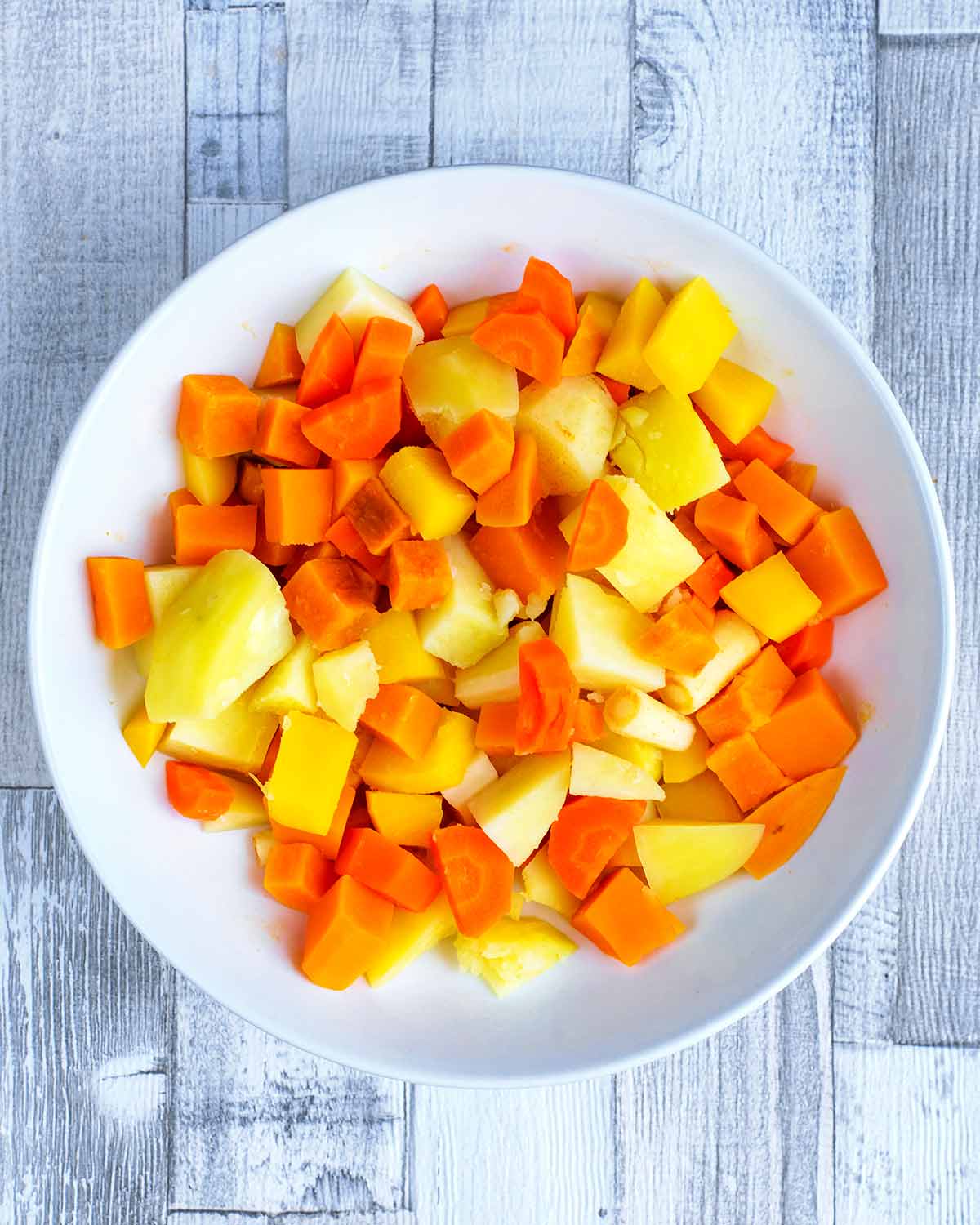 A selection of cooked root vegetables chopped into cubes in a white bowl.