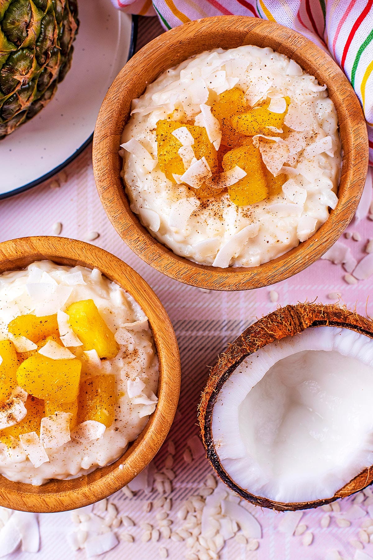 Two wooden bowls of coconut rice pudding topped with pineapple chunks.