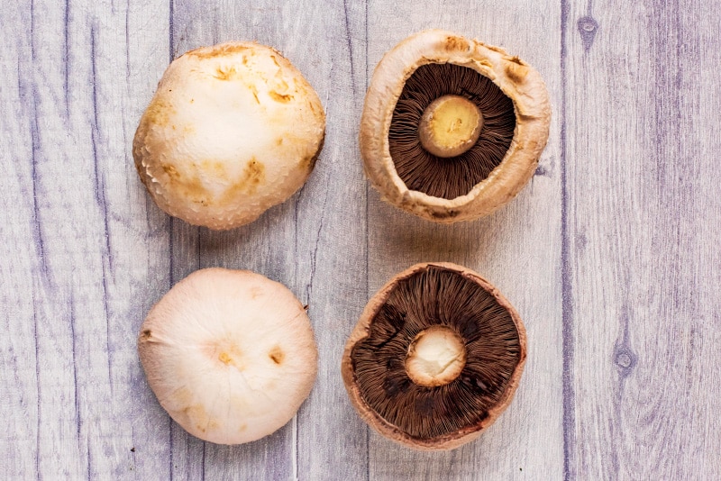 Four Portobello mushrooms on a wooden surface.