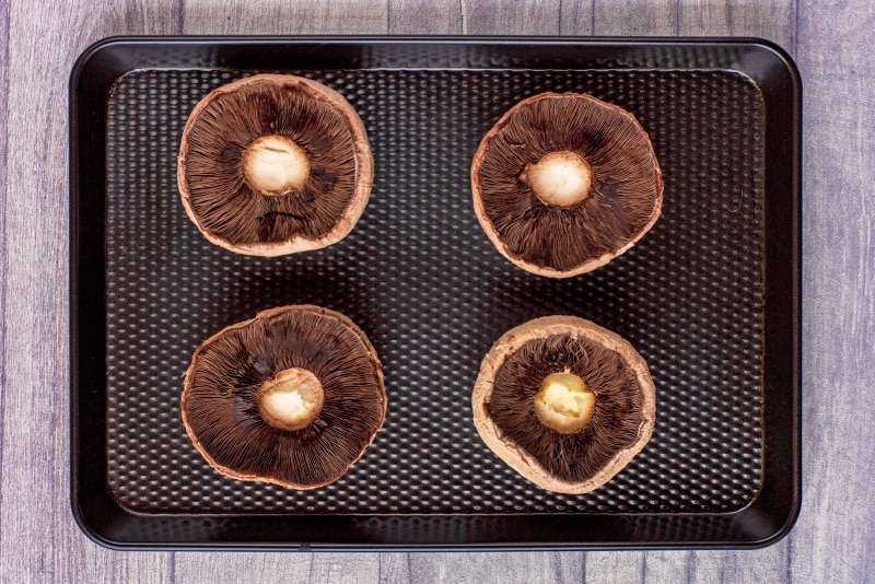 Four Portobello mushrooms on a black baking tray.
