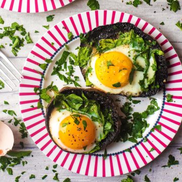 Eggs Baked in Portobello Mushrooms sat on a red and white plate.
