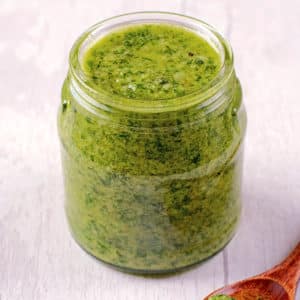 A jar of mixed herb pesto on a wooden surface.