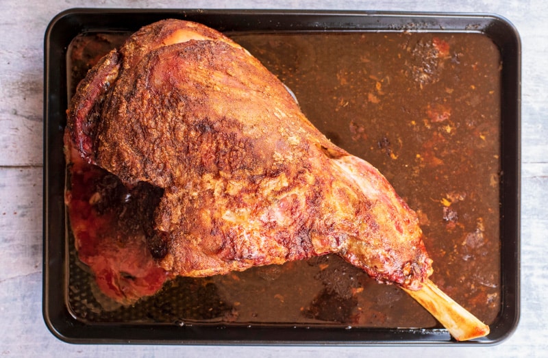 A cooked leg of lamb on a black baking tray.