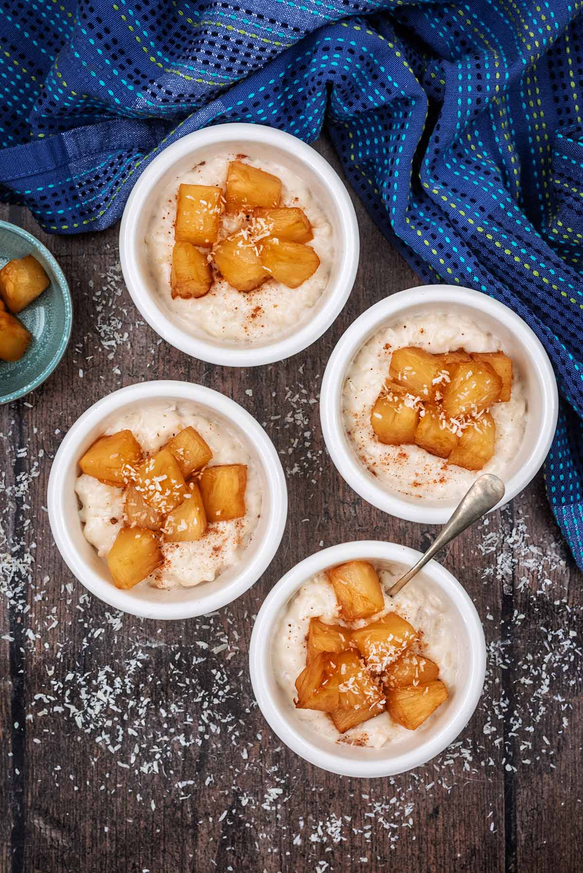 Four ramekins full of rice pudding each topped with caramelised pineapple chunks.