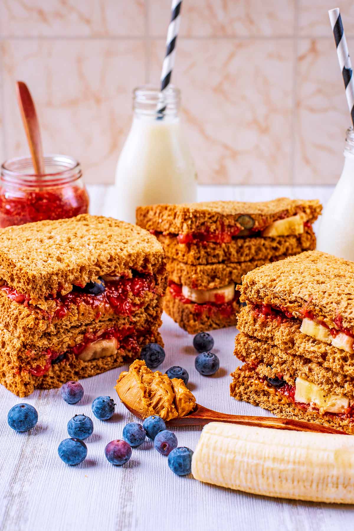 Peanut Butter sandwiches stacked up with two small bottles of milk in the background.