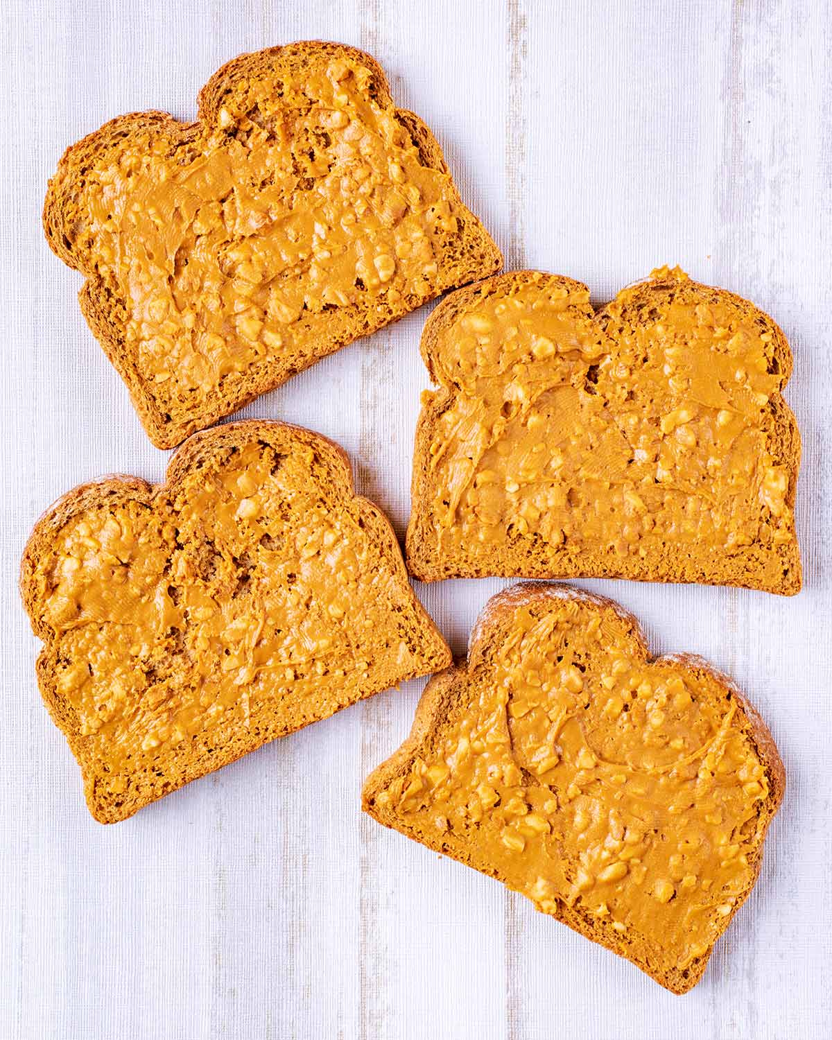 Four slices of brown bread with peanut butter spread over all of them.