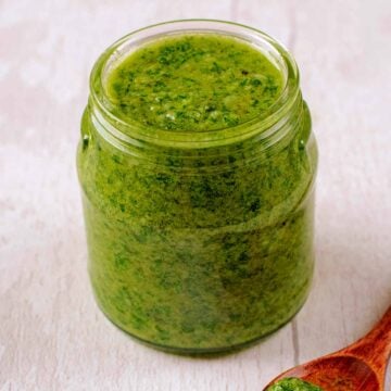 A jar of mixed herb pesto on a wooden surface.
