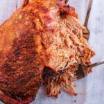 A leg of pulled lamb on a stone coloured surface.