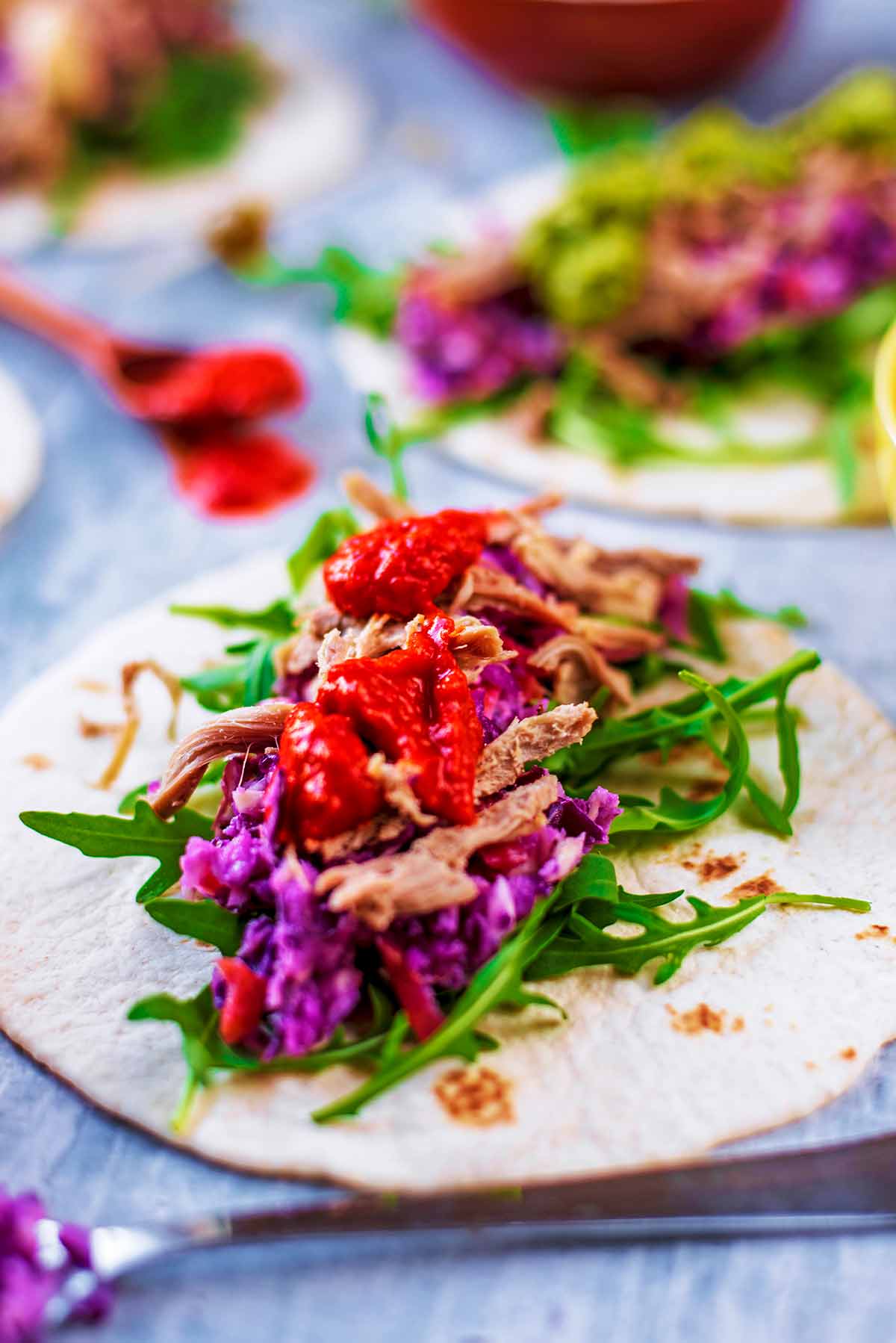 A tortilla wrap topped with lettuce, slaw, pulled lamb and a red sauce.