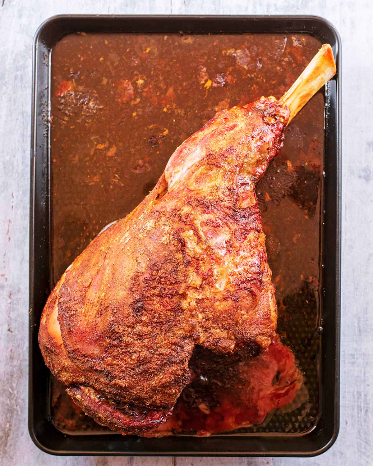 A cooked leg of lamb on a black baking tray.