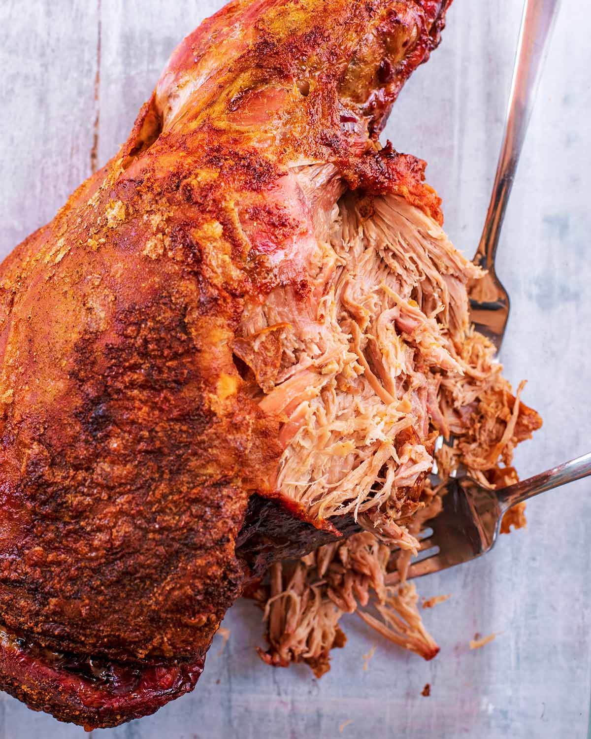 A cooked leg of lamb being pulled apart with forks.