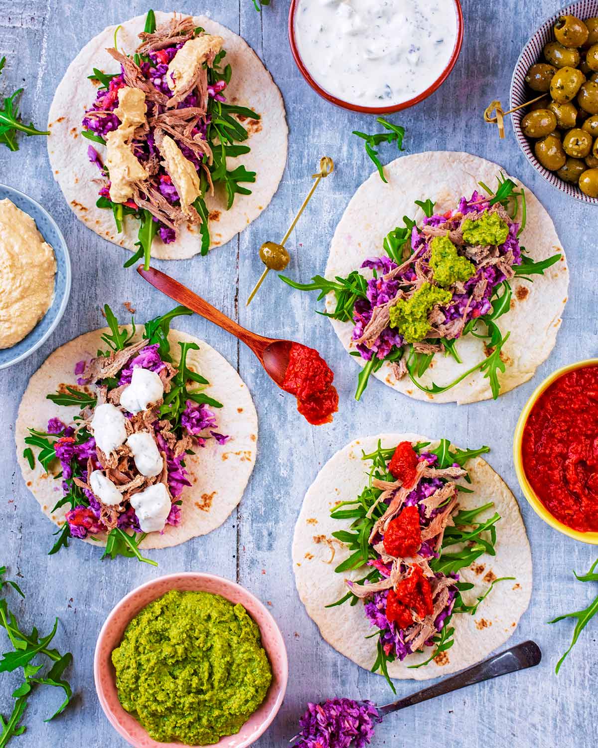 Pulled lamb and toppings on small flour tortillas next to bowls of dip.