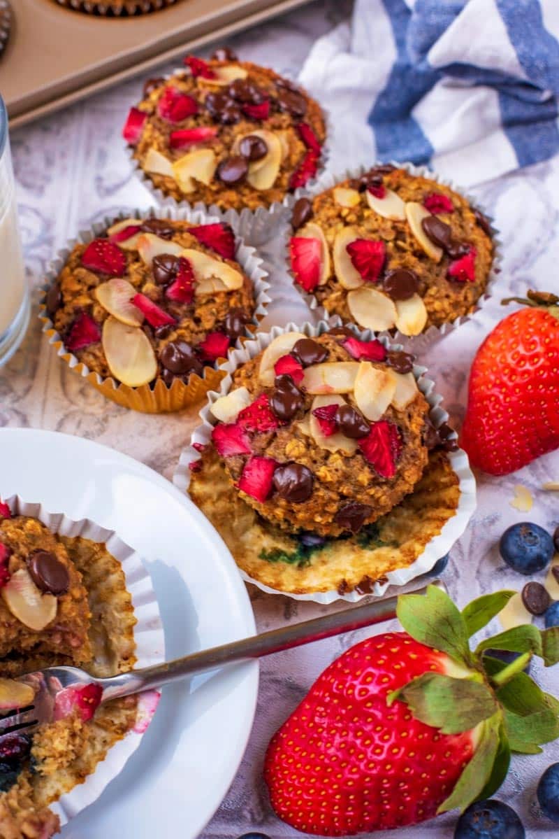 Four Banana Oat Muffins on a table next to another muffin on a plate.