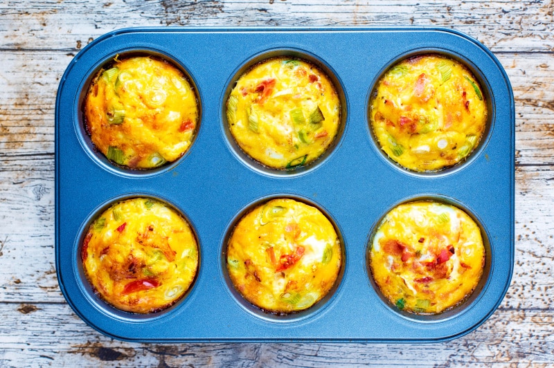 A six hole muffin tin with each hole containing a cooked breakfast egg muffin.