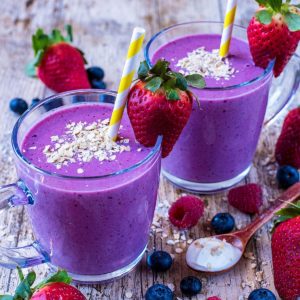 Two glasses of Triple Berry Oat Smoothie surrounded by fresh berries