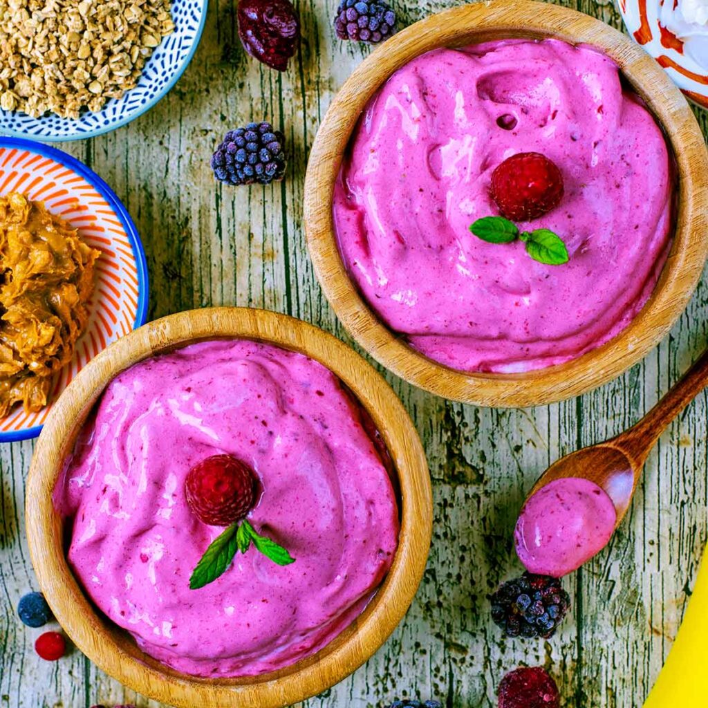 Healthy Frozen Yogurt in two wooden bowls topped with raspberries and mint leaves.