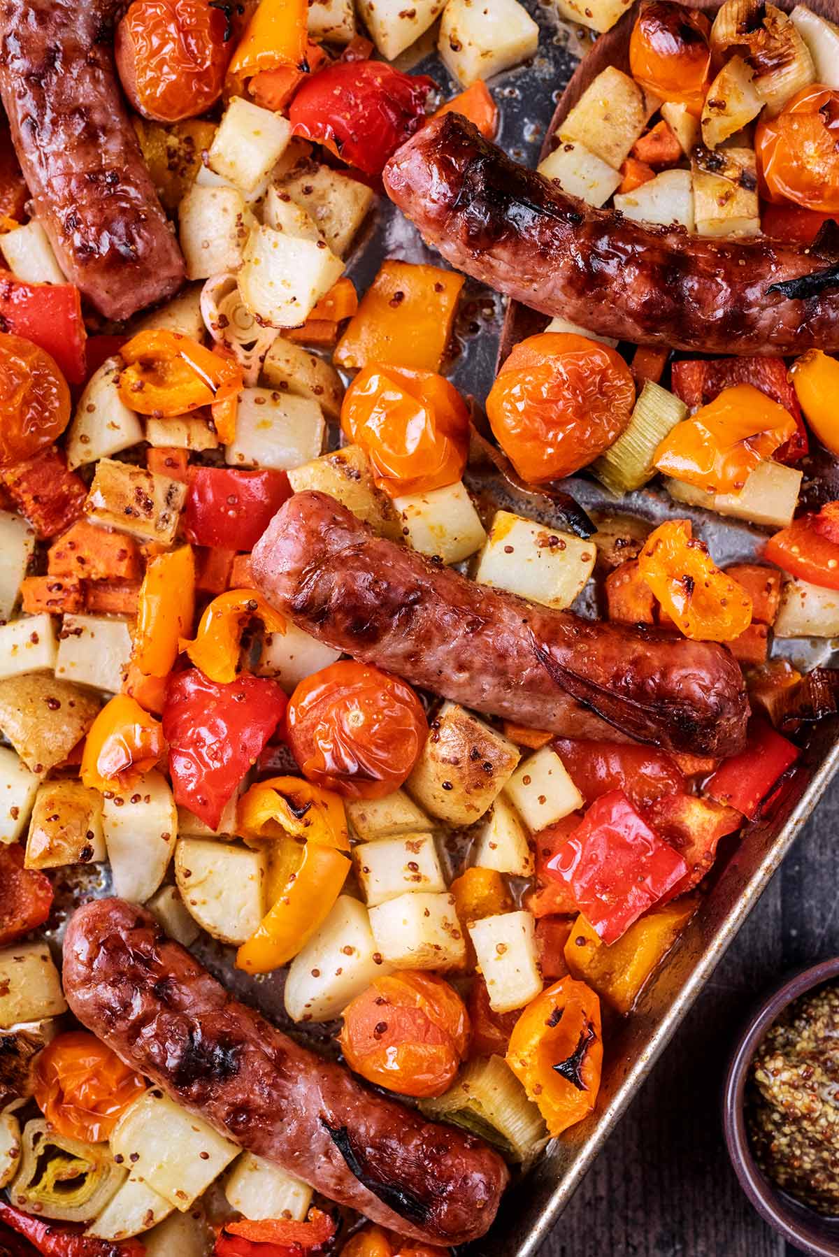 Cooked sausages and vegetables on a baking tray.