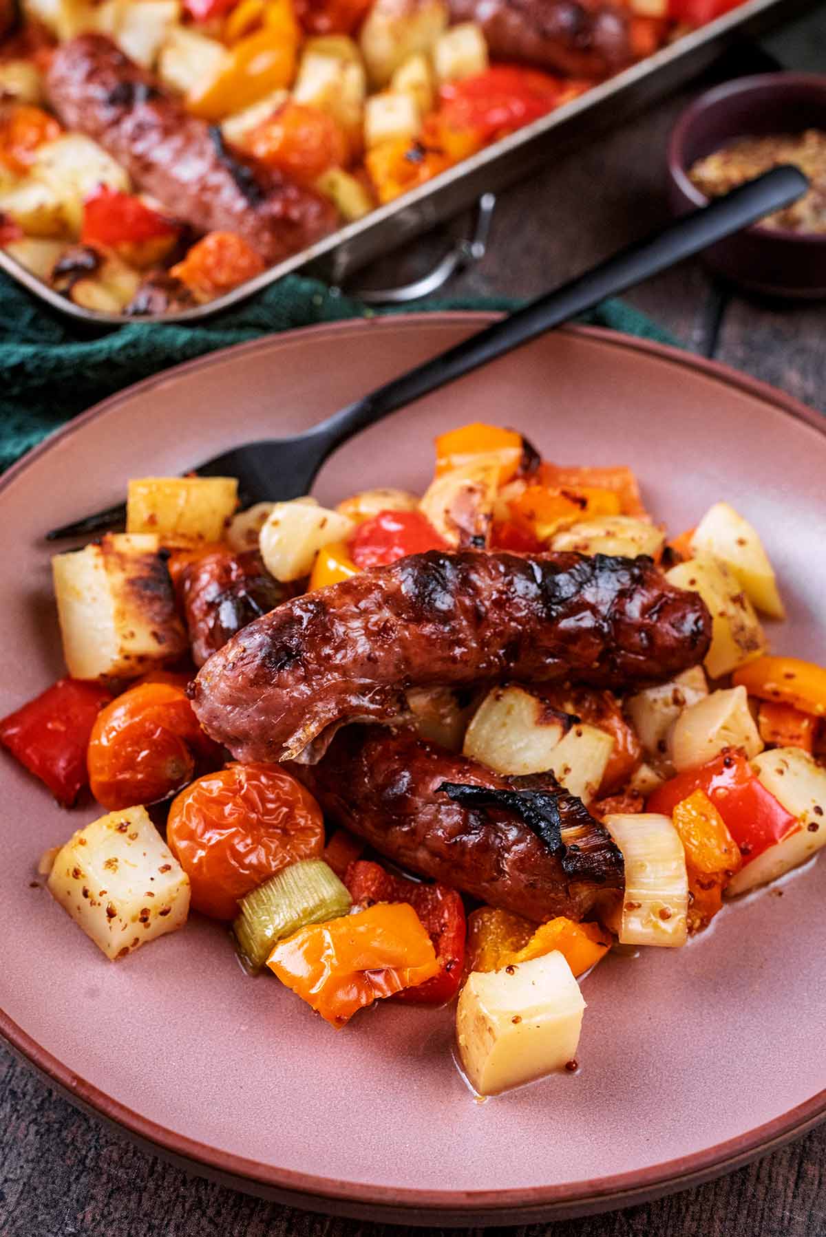 A plate of cooked chopped vegetables and two sausages.