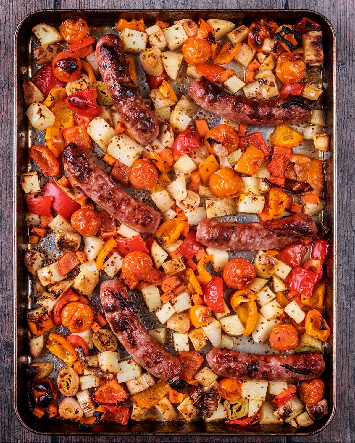 Cooked vegetables and sausages on a baking tray.