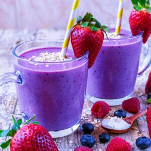 Two glasses of Triple Berry Oat Smoothie surrounded by fresh berries.