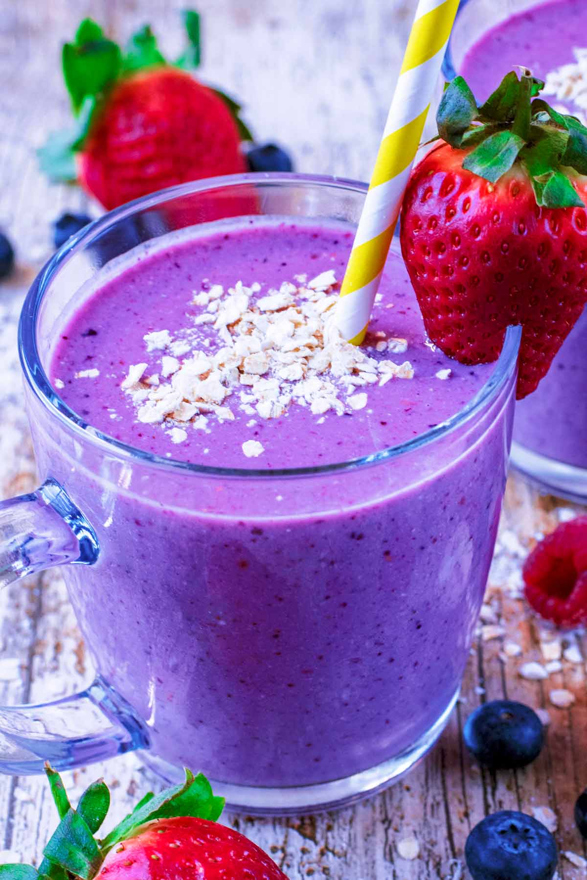 A glass containing a berry smoothie with oats on top and a strawberry on the rim.
