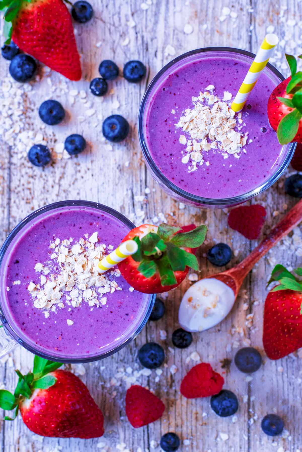Oats and strawberries on top of two glasses of purple coloured smoothies as viewed from above.