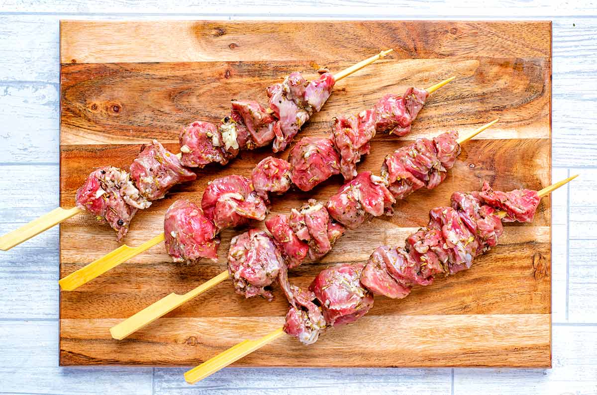 Four wooden skewers with marinated lamb threaded onto them.