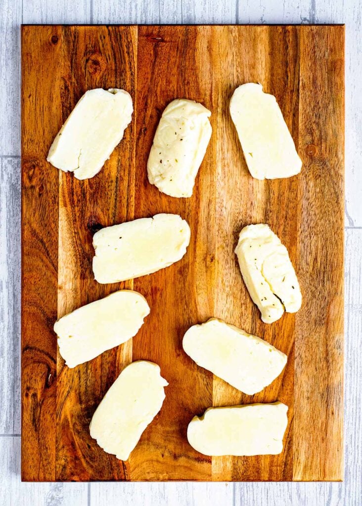 Nine slices of halloumi on a wooden chopping board.