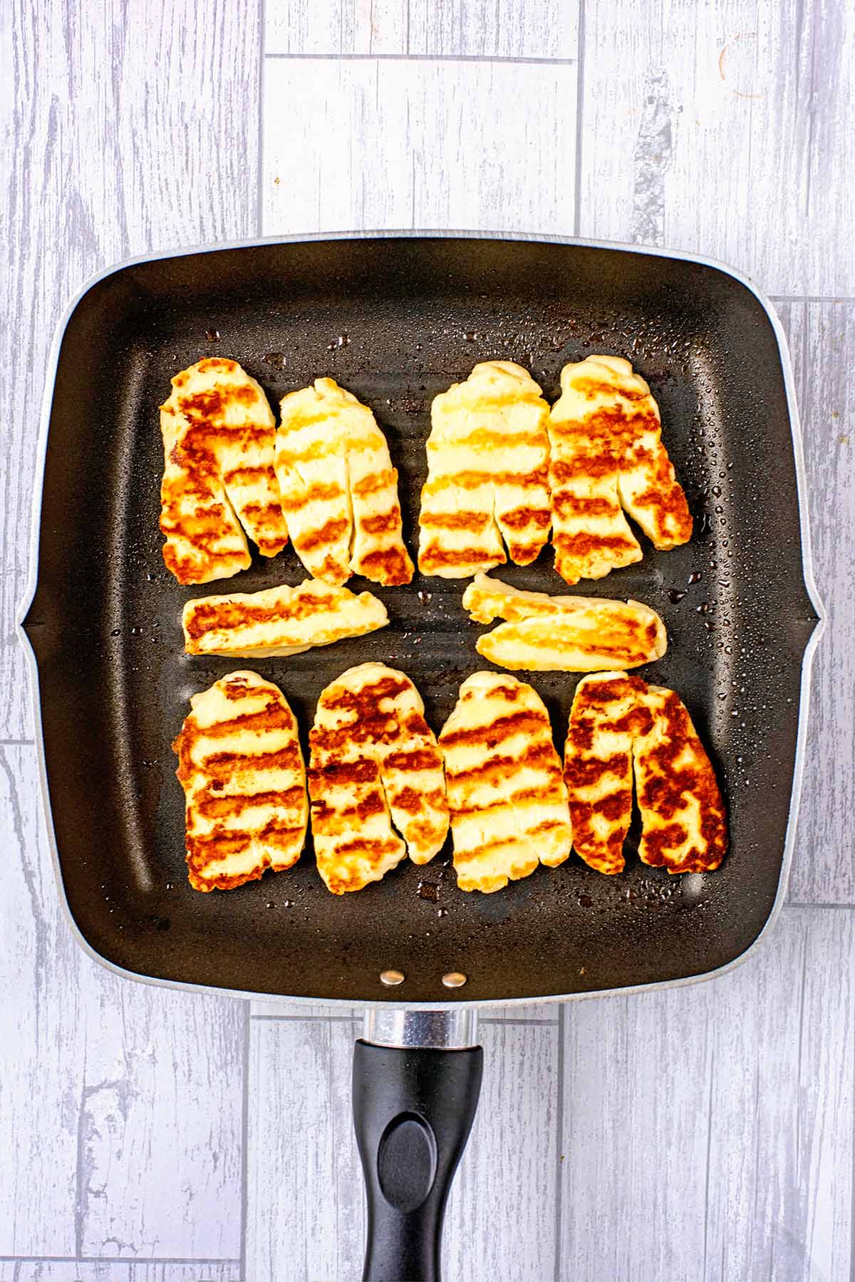 Sliced halloumi cooking in a griddle pan.