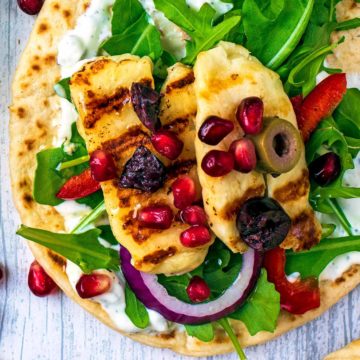 Grilled Halloumi Greek Flatbreads on a wooden surface with pomegranate seeds scattered around.