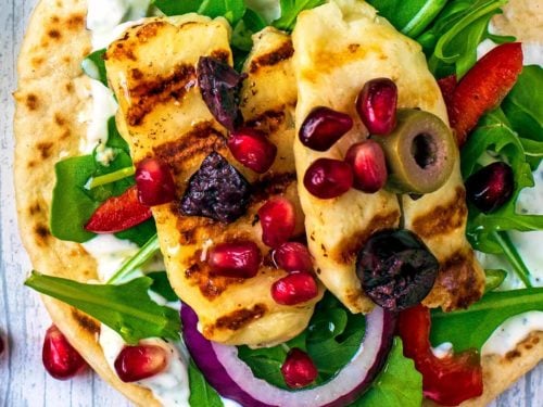 Grilled Halloumi Greek Flatbreads on a wooden surface with pomegranate seeds scattered around.