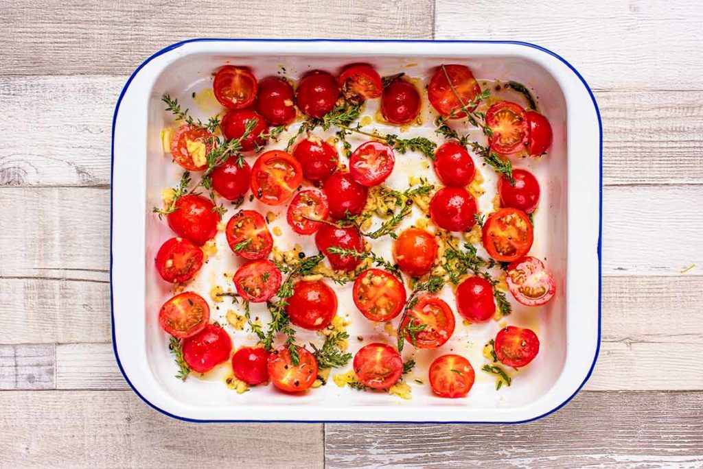 Whole cherry tomatoes, oil and sprigs of thyme in a baking tray.