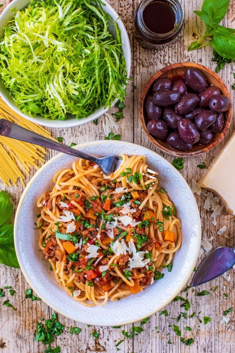 Slow Cooker Spaghetti Bolognese with a bowl of salad and some black olives.